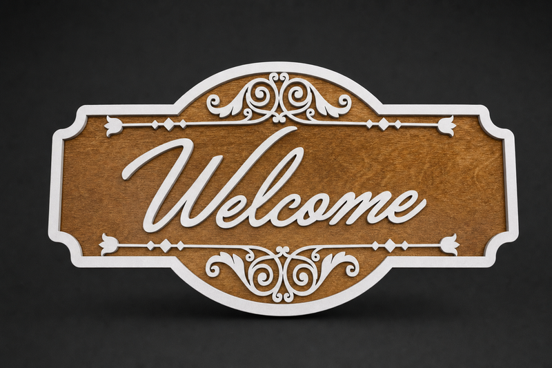Layered wood Welcome sign with cursive script, white scrollwork, and ornate border over a honey-stained panel